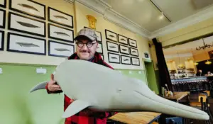 Der Künstler Jörg Mazur hält eine Wal-Skulptur im Arm.